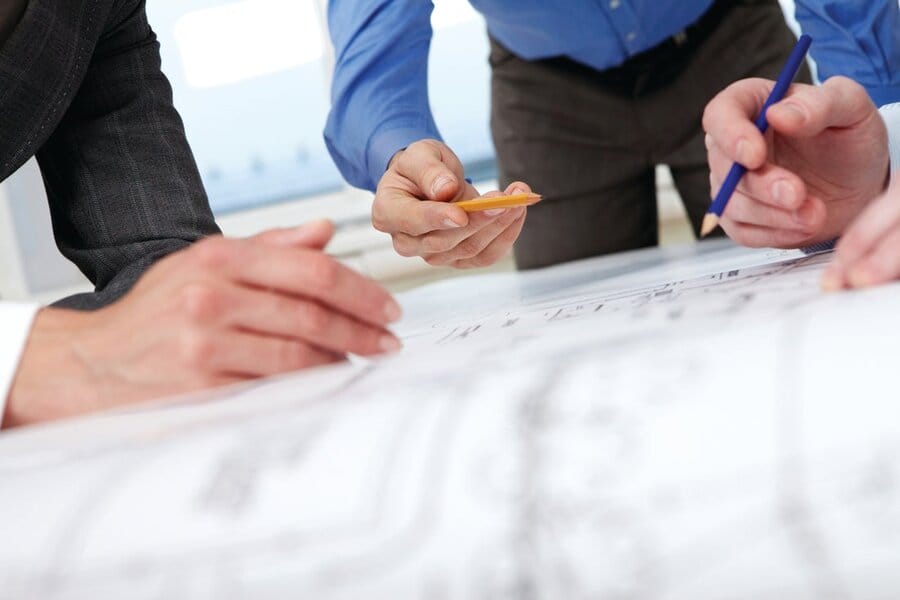 A group of workers standing around and hunched over blueprints and plans on a table.