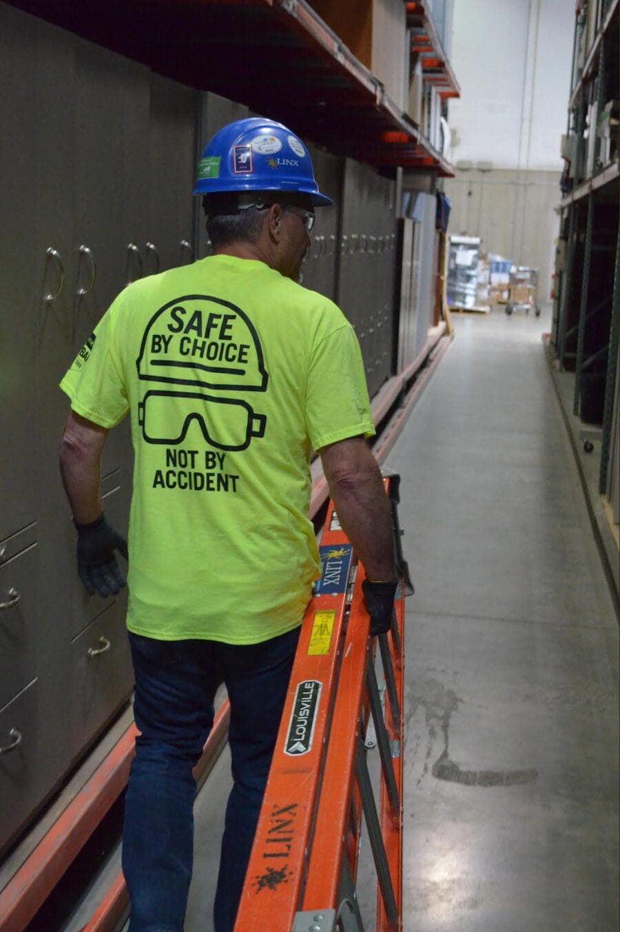 construction worker in bright yellow shirt safely walks in a hallway with a ladder.