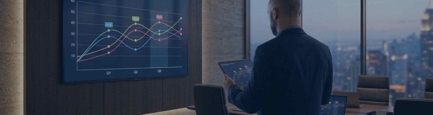 Businessman reviewing performance data on a tablet and large display in a conference room