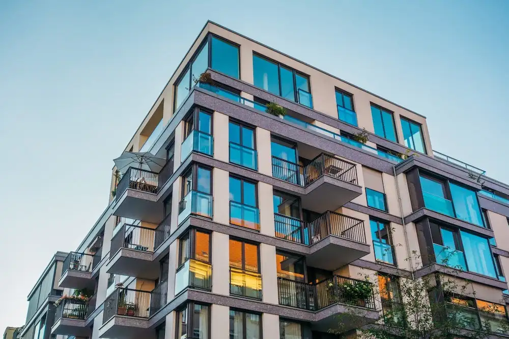 Contemporary mid-rise residential building with teal glass balconies against a clear sky
