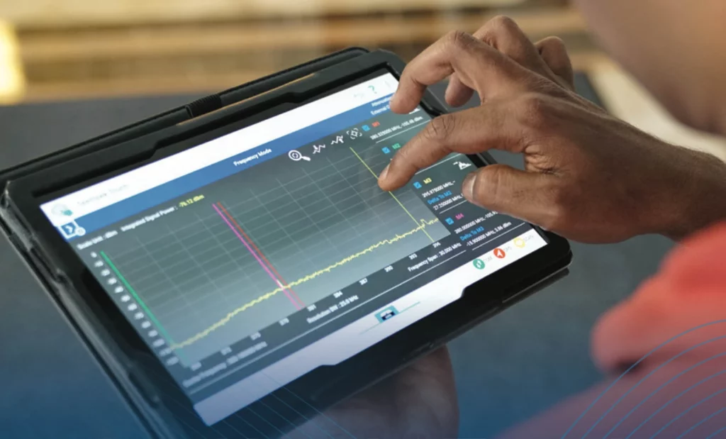 Hands holding a tablet running wireless site survey software, showing live signal measurement data